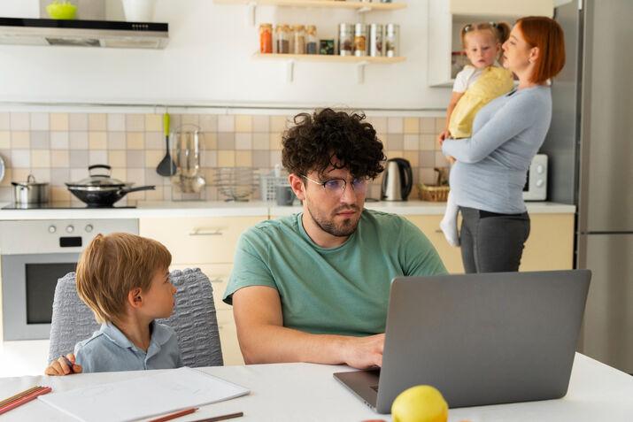 Adult male planning a family trip on laptop with kids and partner nearby – ESL first conditional lesson context.