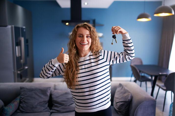 Young woman holding keys in her new rented flat, celebrating moving into a new apartment rental, B1-B2 ESL lesson concept.